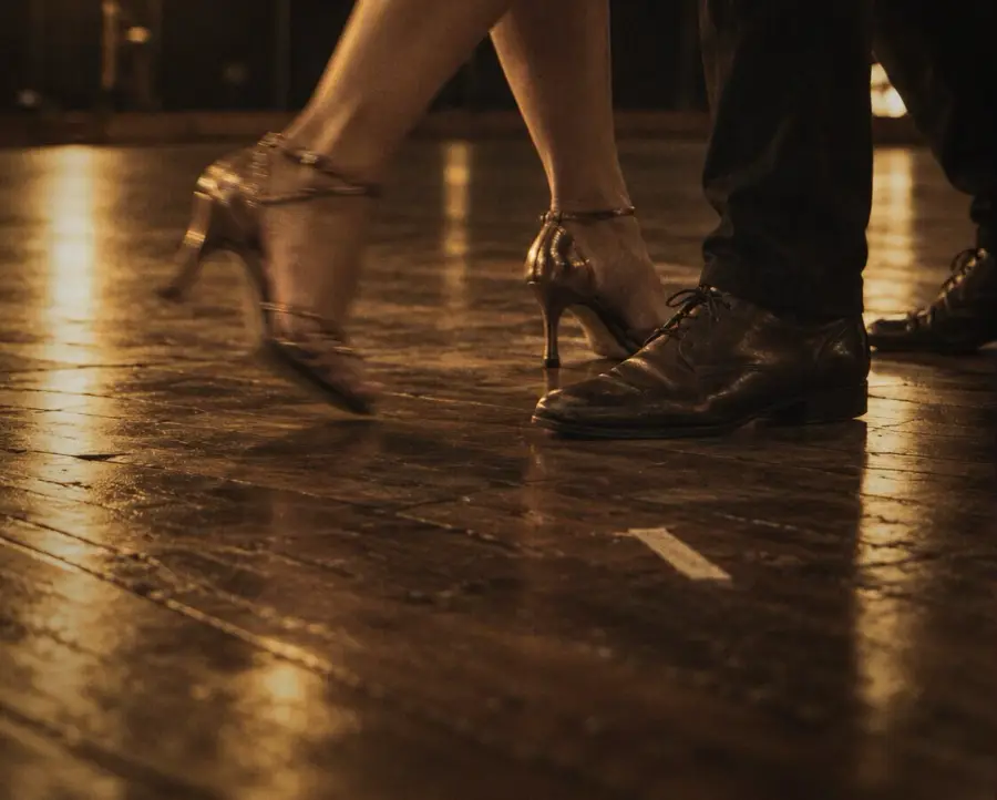 Two dancers' feet on a wooden floor, in warm stage light